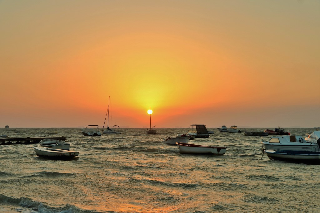 Sol y mástil
En medio del temporal de levante en el Mar Menor, el sol naciente coincide con el mástil de una barca, con el efecto óptico de parecer clavado al palo y hacer de lámpara con un destello que se esparce hacia el horizonte.

