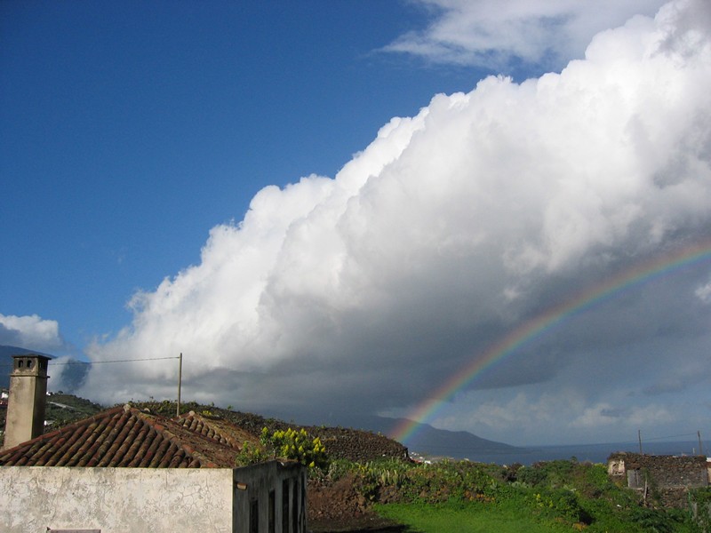 Cumulo arqueado
Cúmulo y arco iris "paralelos".
En contra de lo que pudiera parecer a simple vista, la precipitación que da lugar a la formación del arco iris no procede del cúmulo de la fotografía, sino de otras nubes situadas más a la izquierda , nubes orográficas "enganchadas" a las cumbres de la isla de La Palma, y desde las que el viento arrastra la precipitación hasta el lugar hacia donde se observa el arco iris.
Por su parte, el cúmulo de la imagen está en una onda de montaña a sotavento.
