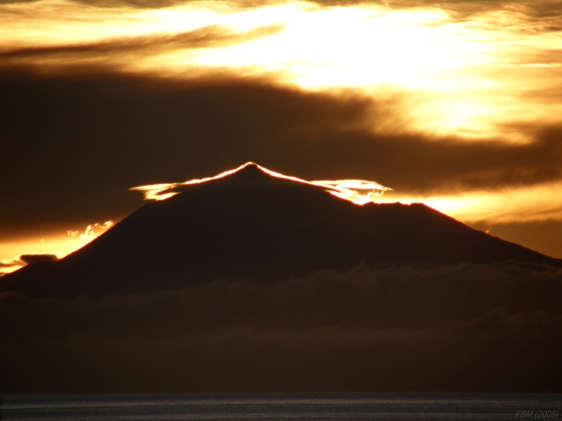 Nube capuchón sobre el Teide al contraluz
Nube capuchón al amanecer marcando la silueta del Pico del Teide al verse iluminada al contraluz sobre el fondo oscuro del yunque de un viejo cumulonimbo. 
La foto está tomada con zoom óptico 18x, desde la isla de La Palma, a más 100 km de distancia.  
Álbumes del atlas: nubes_capuchon