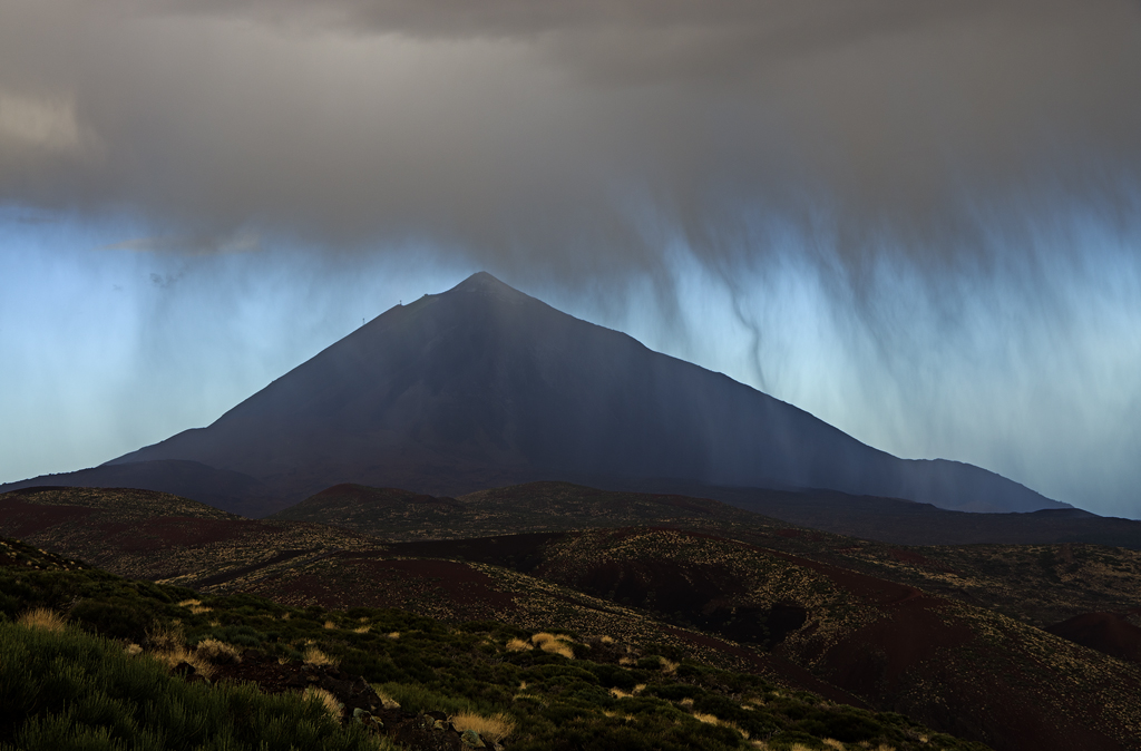 Praecipitatio
En la foto observamos nubes medias sobre el Parque Nacional del Teide descargando cortinas de precipitación que no logran ocultar completamente la silueta del pico más alto de España, el Teide.

