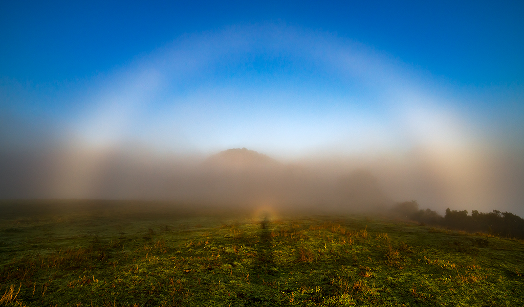 Arco de niebla con Espectro de Brocken
El Valle de Sau al amanecer estaba cubierto de niebla, pero más tarde con el sol bajo y la niebla esparciéndose, pude captar este doble fenómeno meteorológico; el arco de niebla coronando el montículo del fondo i en el centro el Espectro de Brocken.
