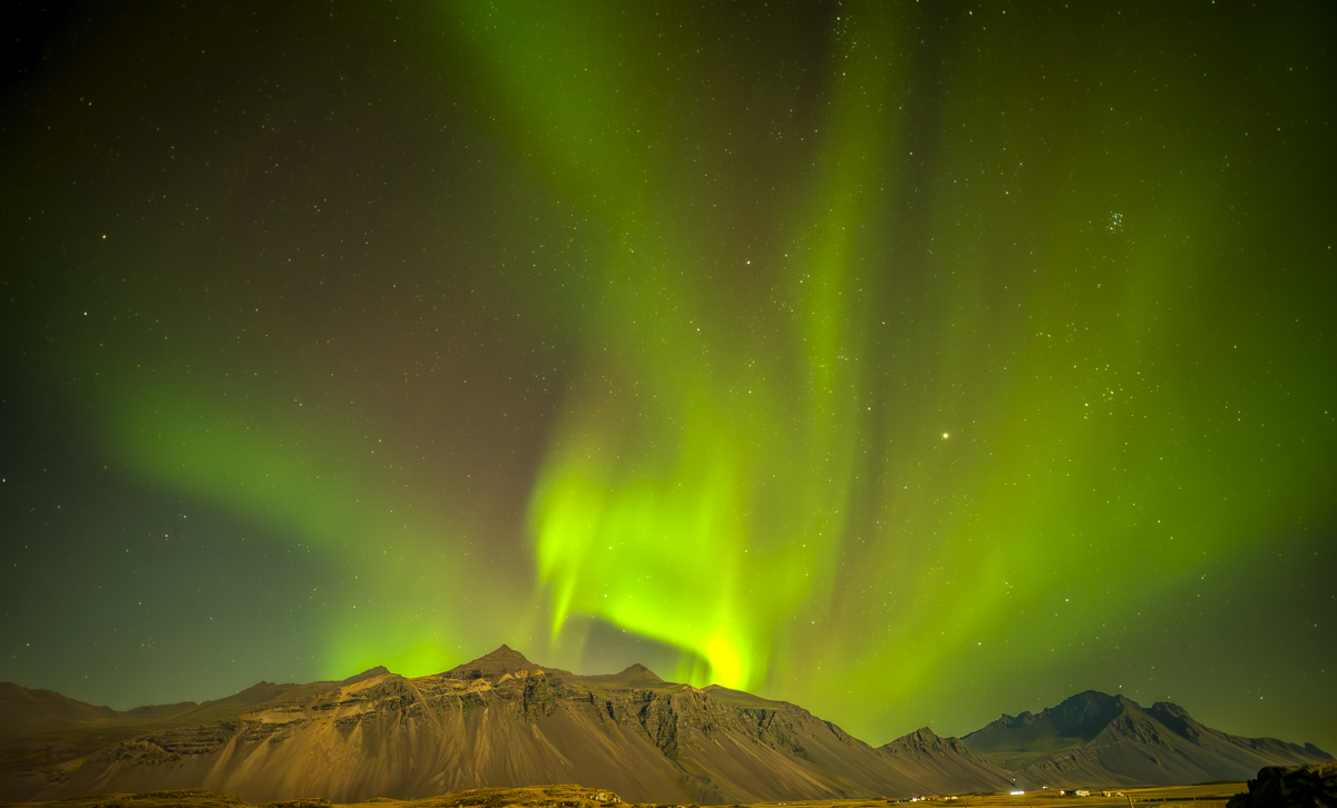 LA LUNA CASI LLENA ILUMINA LAS GRANJAS ISLANDESAS AL PIE DE LAS MONTAÑAS MIENTRAS UNA AURORA ROJA Y VERDE LLENA EL CIELO  DE COLORES...
