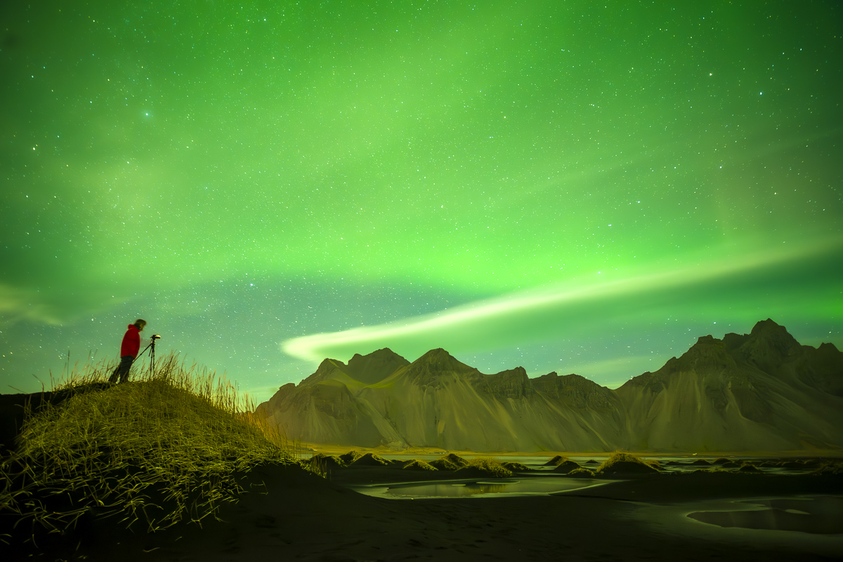 una nubes lenticular  se  sitúa sobre al montaña d eVestrahorn en Islandia mientras  la aurora boreal ilumina el cielo de verde 
