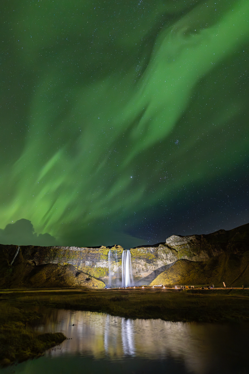 Cascada de Islandia, de las mas famosas, iluminada por la noche, con aurora sobre ella y su reflejo
