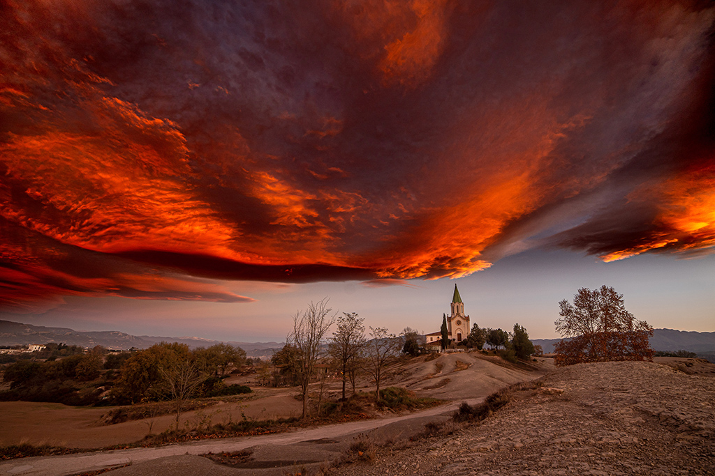 Cielo en llamas de tonos cálidos al amanecer. Un instante efímero donde la naturaleza y la arquitectura se funden en un cuadro celestial.
