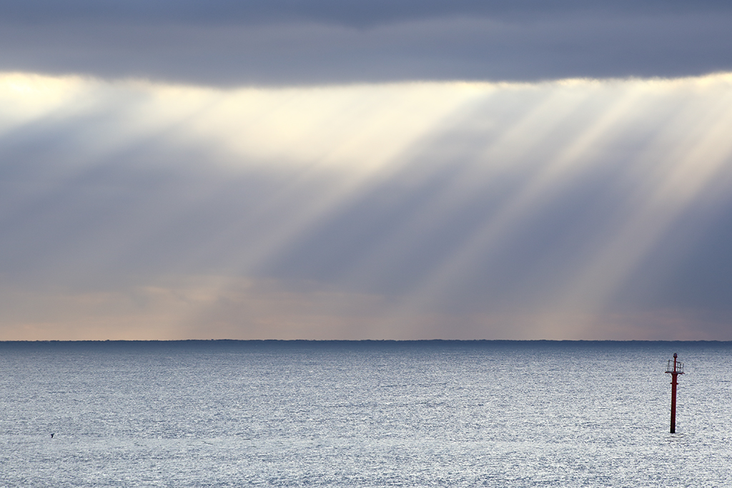 Cortina de rayos en el horizonte
Los rayos solares comienzan a filtrarse a través de una definida línea entre las espesas nubes después de una noche de tormenta y forman una cortina de rayos diagonales en el horizonte. 
