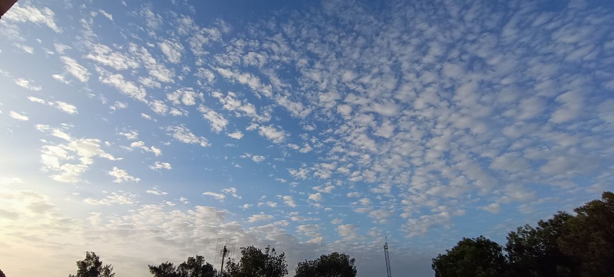 Nubes como motas de polvo esparcidas por el cielo, captadas en una azotea de veraniego.
