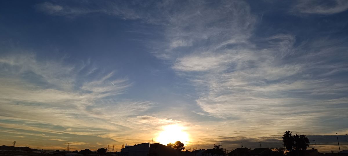 2 columnas de nubes con forma similar a humo yendo en la misma dirección, regados por la luz del atardecer.
