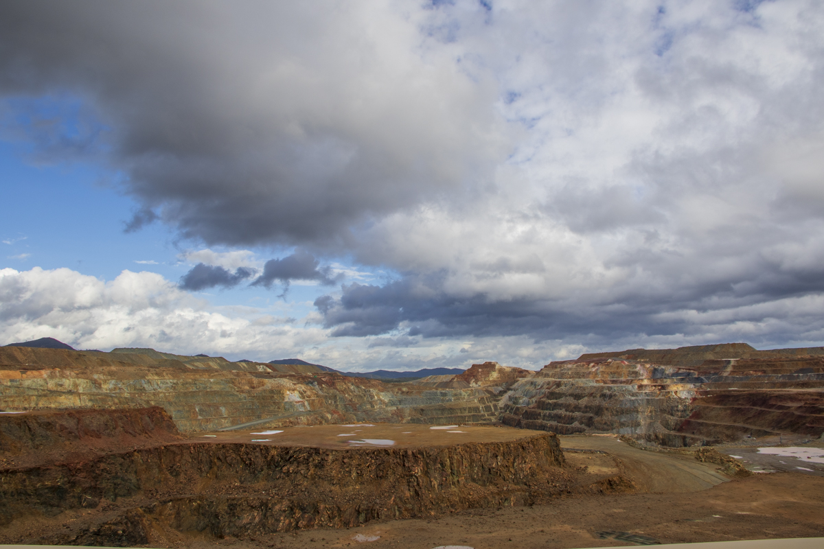 Bajo un manto de nubes densas y sombrías, la vasta extensión de una mina a cielo abierto revela la magnitud de la intervención humana en la naturaleza. Los estratos de tierra y roca, marcados por el paso del tiempo y la extracción incesante, contrastan con el cielo cambiante que anuncia la inminencia de una tormenta. Esta imagen captura el dramático encuentro entre la mano del hombre y los elementos, un recordatorio visual de la vulnerabilidad del equilibrio natural.
