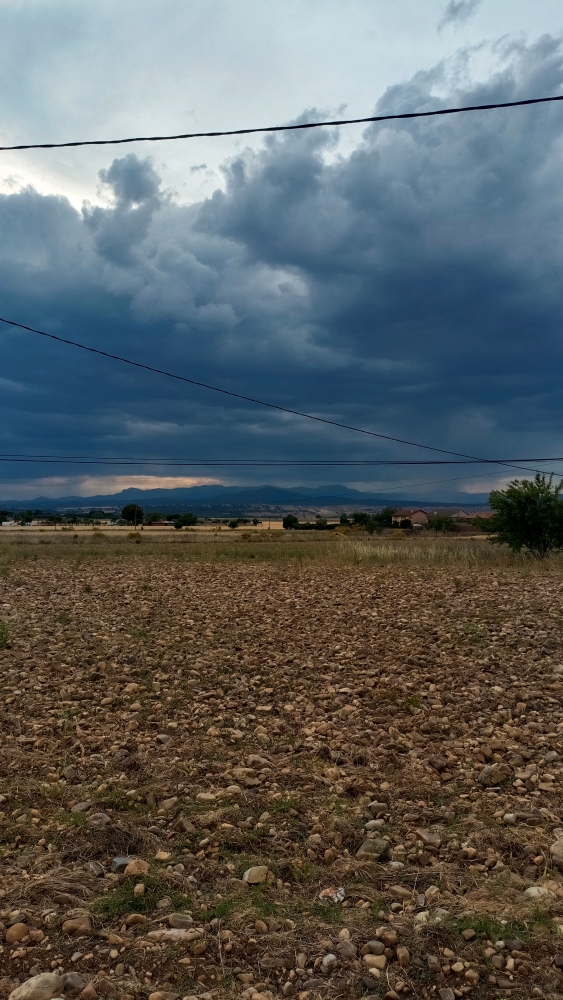 Estaba dando un paseo por mi pueblo y como se ve en el panorama en este caso si lloviendo al fondo con un atardecer bonito en la sierra y unas nubes tormentosas. Crea este paisaje casi infernal, limitando entre la claridad y la oscuridad.
