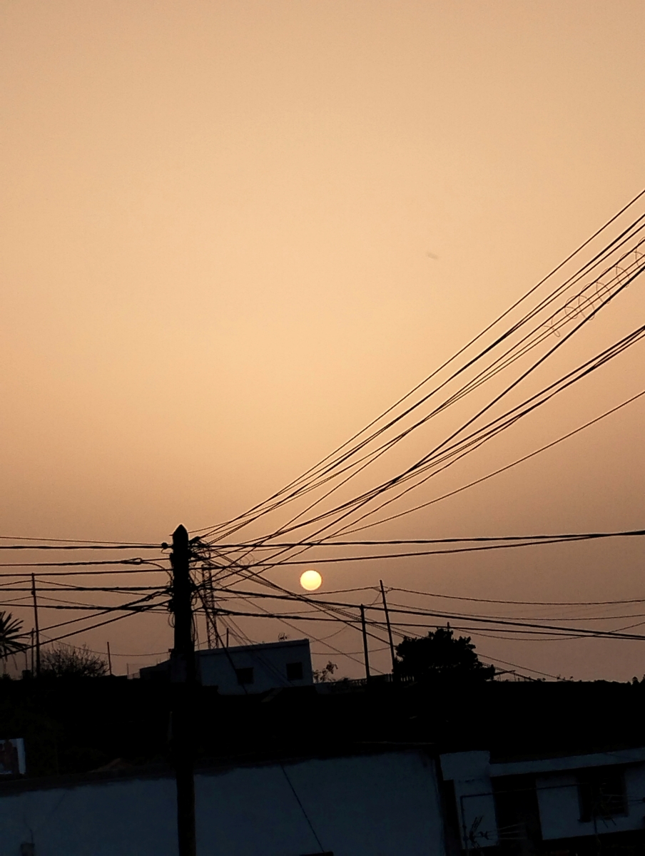 Una tarde dorada donde el sol se esconde detrás de los cables de electricidad
