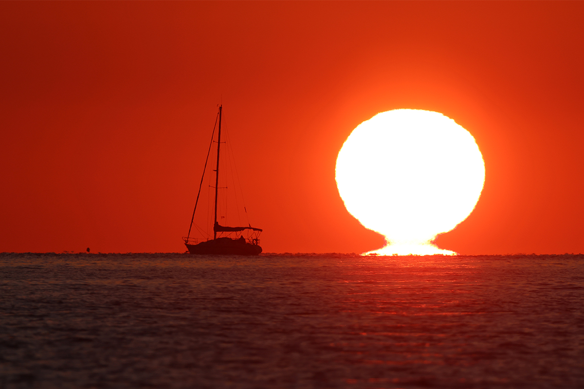 Sortida de sol amb efecte omega o gerro i el vaixell pasquer mirant-lo
