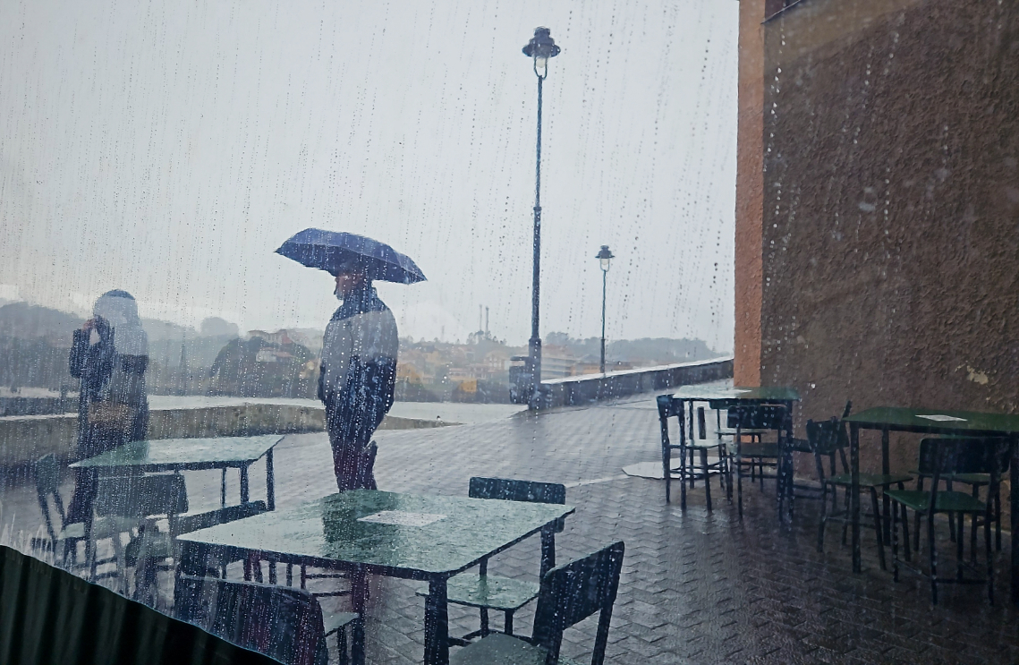 Terraza de bar con personas bajo la lluvia y tras una cortina de plástico.
