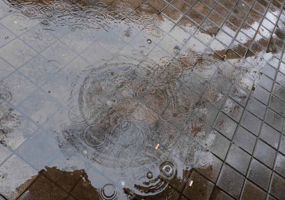 Gotas de lluvia cayendo sobre un charco en acera con restos de cigarrillos
